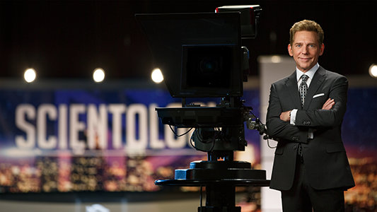 David Miscavige in Hollywood, California, medium, wearing dark gray suit next to camera in studio