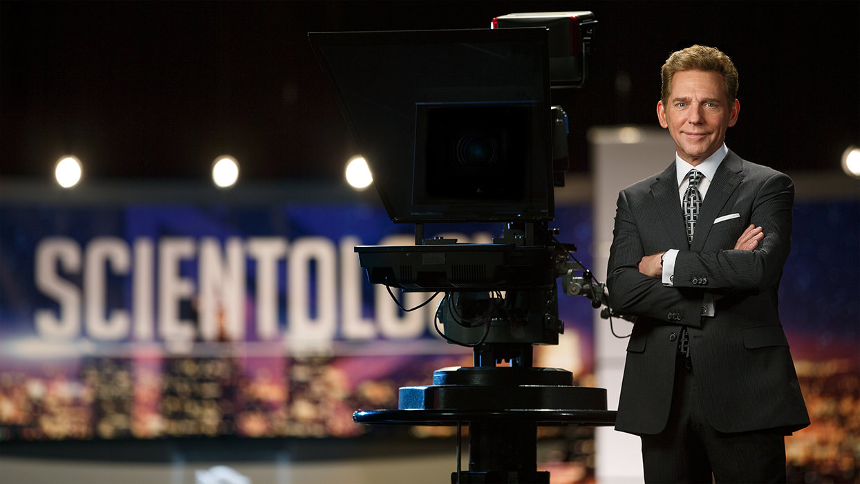 David Miscavige in Hollywood, California, medium, wearing dark gray suit next to camera in studio